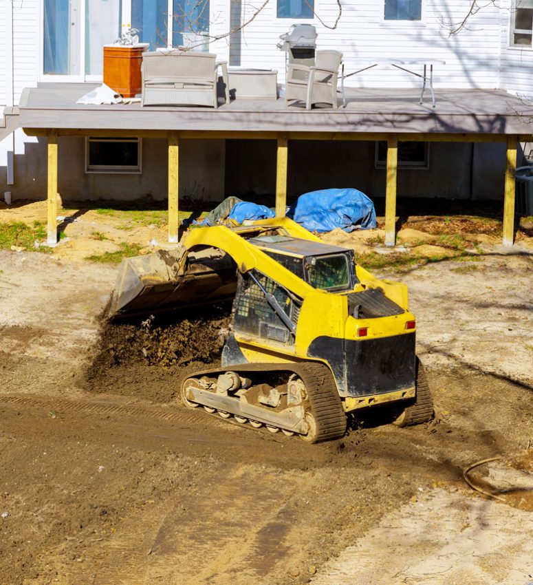 An ongoing grading work; a bulldozer moving a mass of soil in the backyard of a house.