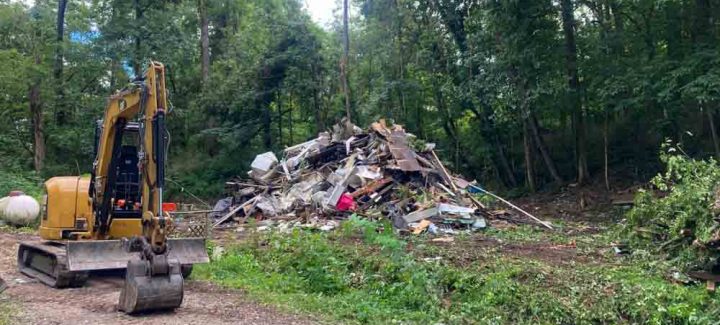 A large pile of mixed debris, including concrete, wood, and metal, in the middle of a forest.